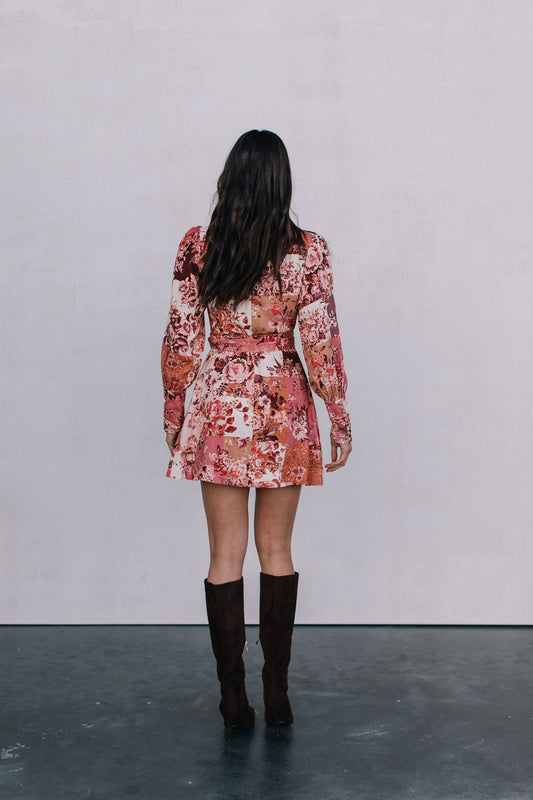 Person wearing a floral dress with long sleeves and knee-high boots on a plain background