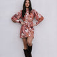 Woman wearing a floral dress and black knee-high boots against a white wall.