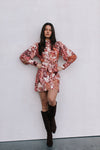 Woman wearing a floral dress and black knee-high boots against a white wall.