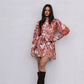 Woman wearing a floral dress with long sleeves and black knee-high boots against a plain background