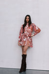 Woman wearing a floral dress with long sleeves and black knee-high boots against a plain background