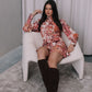 Woman in a floral dress and knee-high boots sitting on a white chair.