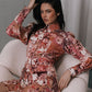 Woman in a floral dress sitting on a white chair against a gray wall.