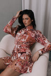 Woman in a floral dress sitting on a white chair against a gray wall.