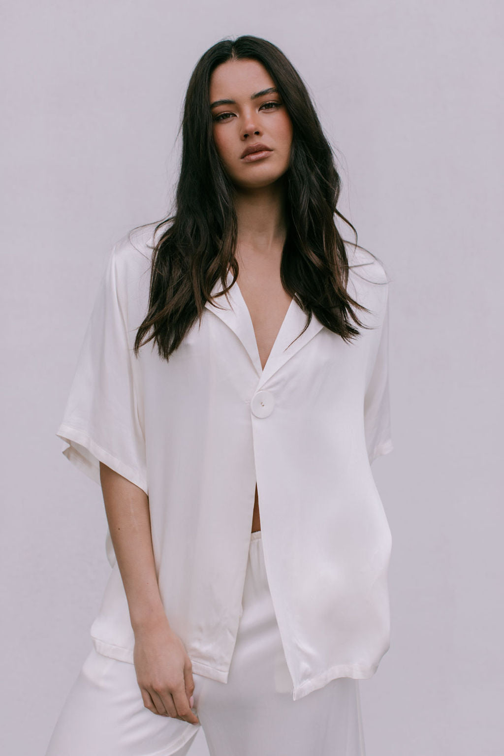 Woman wearing a white blouse and pants against a plain background