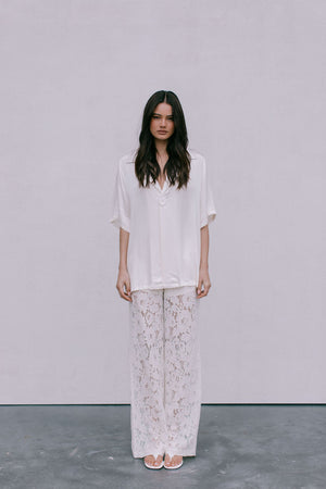 Woman wearing a white blouse and floral pants against a plain background