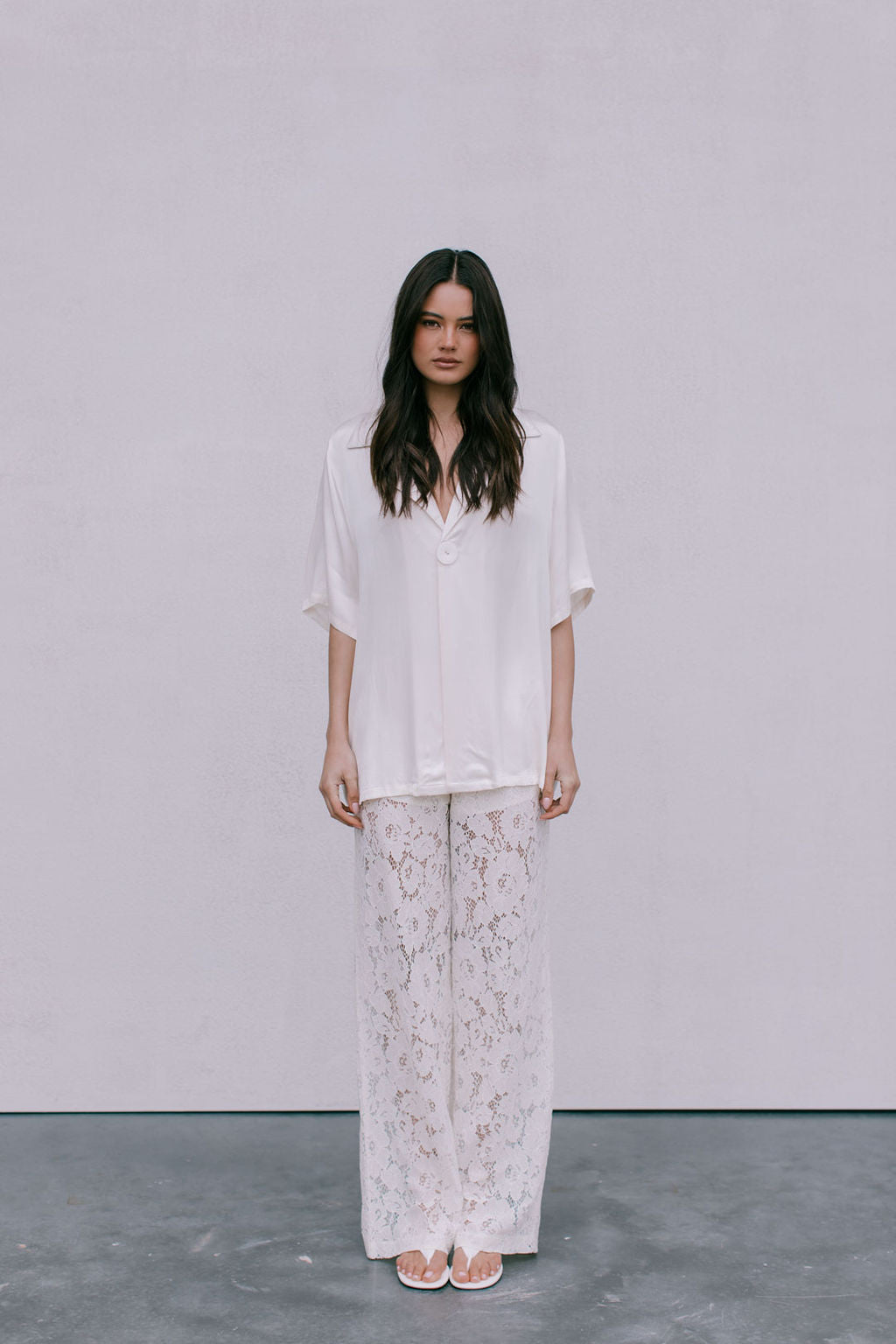 Woman wearing a white blouse and floral pants against a plain background
