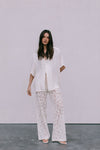 Woman wearing a white outfit with lace pants against a plain background