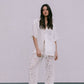 Woman wearing a white shirt and lace pants against a plain background