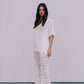 Woman wearing a white outfit with lace pants against a plain background