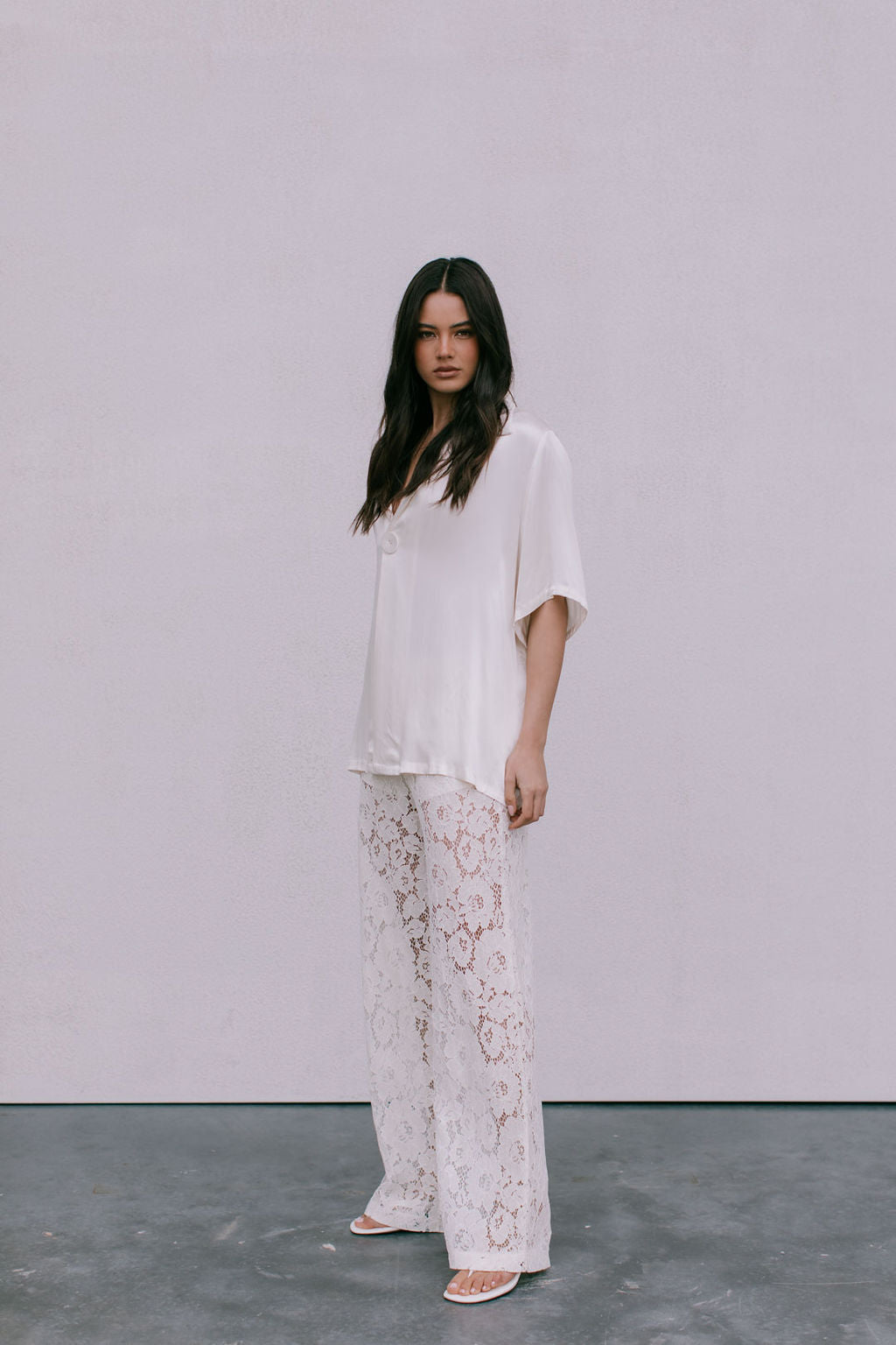 Woman wearing a white outfit with lace pants against a plain background