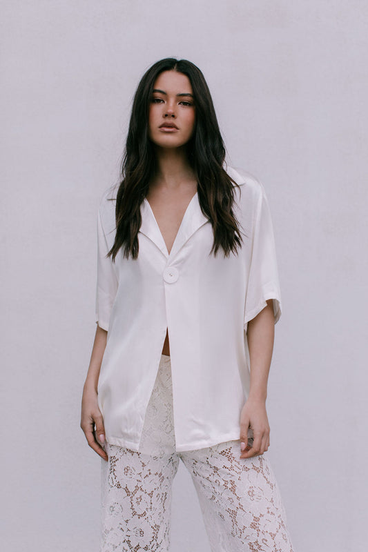 Woman wearing a white blouse and lace pants against a plain background