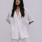 Woman wearing a white blouse and lace pants against a plain background
