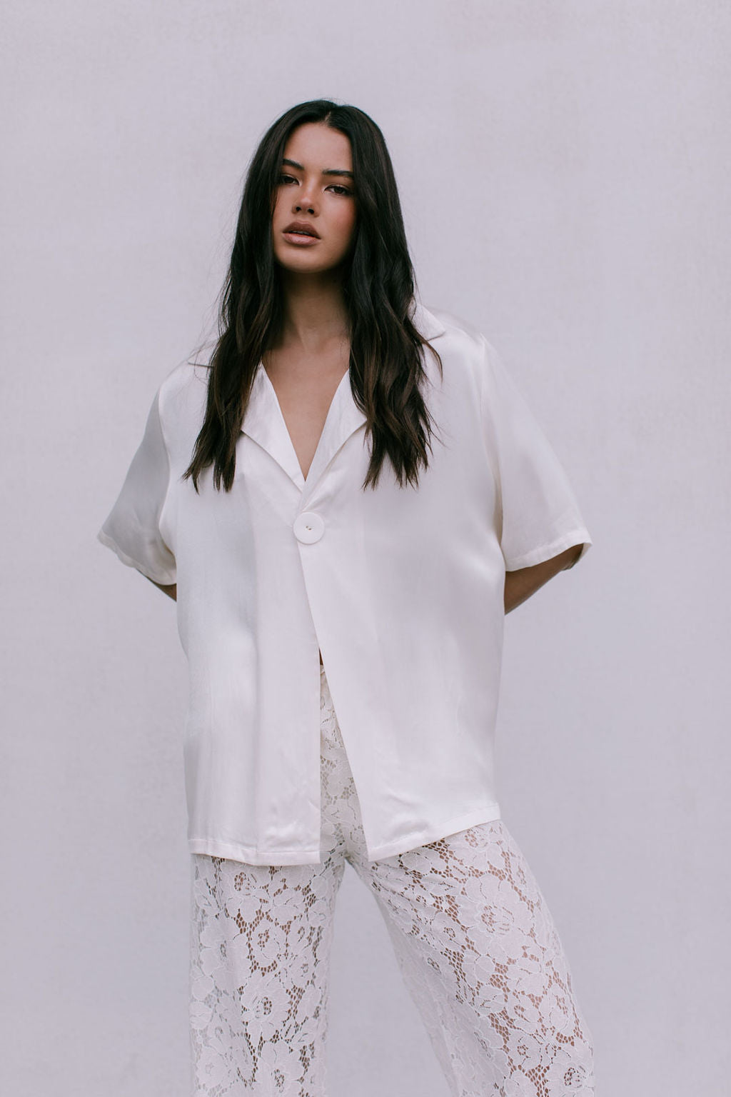 Woman wearing a white blouse and lace pants against a plain background