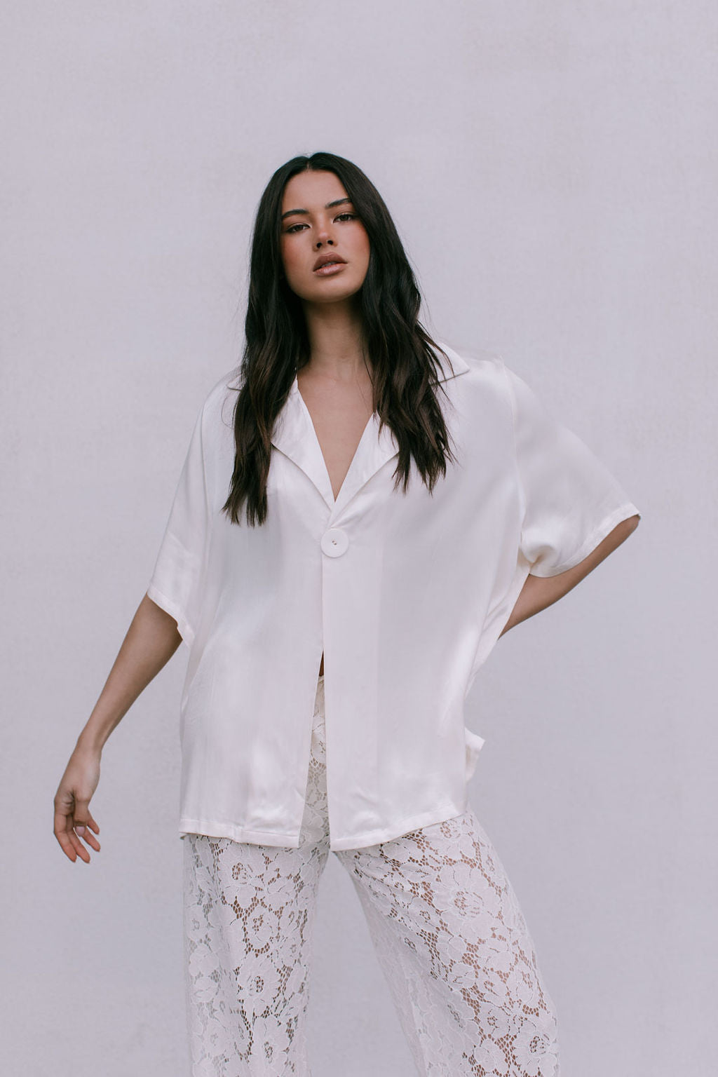Woman wearing a white blouse and lace pants against a plain background