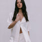 Woman wearing a white satin shirt and lace pants against a plain background