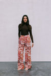 Woman wearing a brown top and floral pants against a plain background