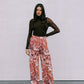 Woman wearing a black top and floral pants against a plain background