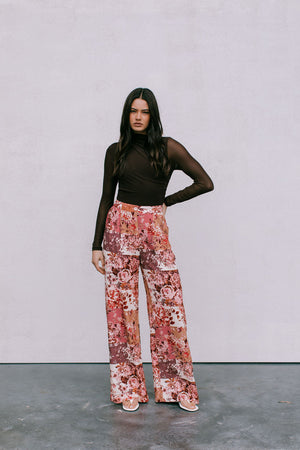Woman wearing a black top and floral pants against a plain background