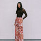 Woman wearing a brown top and floral pants against a plain background