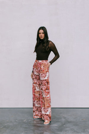Woman wearing a brown top and floral pants against a plain background