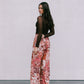 Woman wearing a brown top and floral pants against a plain background