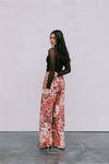 Woman wearing a brown top and floral pants against a plain background