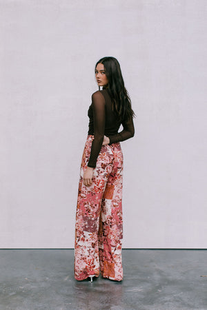Woman wearing a brown top and floral pants against a plain background