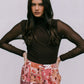 Woman wearing a brown mesh top and floral pants against a plain background