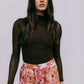 Woman wearing a brown long-sleeve top and floral pants against a plain background