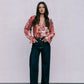 Woman wearing a floral blouse and dark jeans against a plain background