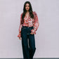 Woman wearing a floral blouse and dark jeans against a plain background