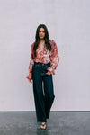 Woman wearing a floral blouse and dark jeans against a plain background