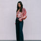 Woman wearing a floral blouse and dark jeans against a plain background