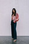 Woman wearing a floral blouse and dark jeans against a plain background