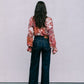 Person wearing a floral blouse and dark jeans standing against a plain background
