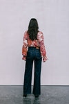 Person wearing a floral blouse and dark jeans standing against a plain background