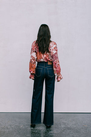 Person wearing a floral blouse and dark jeans standing against a plain background