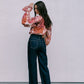 Woman wearing a floral blouse and dark jeans against a plain background