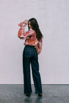 Woman wearing a floral blouse and dark jeans against a plain background