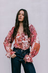 Woman wearing a floral blouse with long sleeves against a plain background