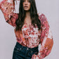 Woman wearing a floral blouse with long sleeves against a plain background