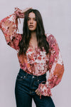 Woman wearing a floral blouse with long sleeves against a plain background