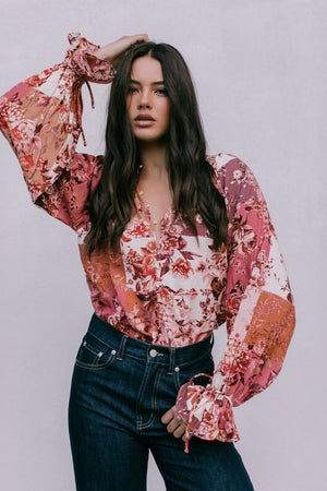 Woman wearing a floral blouse with long sleeves against a plain background