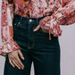 Person wearing a floral blouse with long sleeves and dark jeans against a neutral background