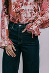Person wearing a floral blouse with long sleeves and dark jeans against a neutral background
