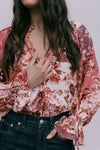 Person wearing a floral blouse with long sleeves and dark jeans on a plain background
