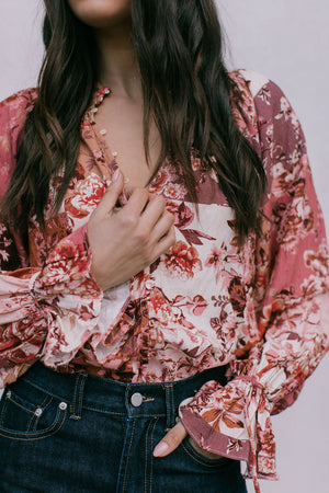 Person wearing a floral blouse with long sleeves and dark jeans on a plain background