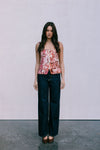 Woman wearing a floral top and dark jeans against a plain background
