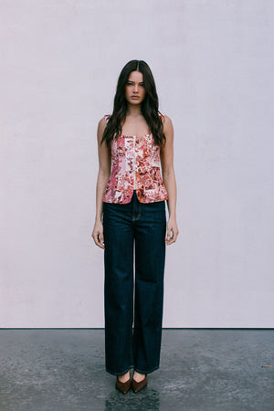 Woman wearing a floral top and dark jeans against a plain background